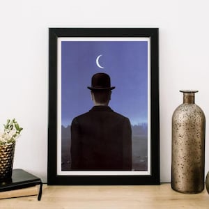 May include: A framed print of a painting depicting a man in a black bowler hat standing with his back to the viewer, facing a crescent moon in a dark blue sky.