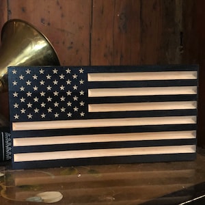 May include: A wooden American flag with a black background and white stars and stripes. The flag is made of wood and has a natural wood finish.