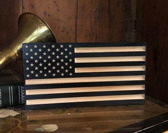 May include: A wooden American flag with a black background and white stars and stripes. The flag is made of wood and has a natural wood finish.