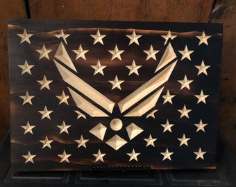 May include: A wooden American flag with a carved United States Air Force emblem in the center. The flag is stained dark brown and the emblem is a light wood color.