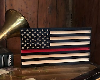 May include: A wooden American flag with a red stripe across the middle, representing the "Thin Red Line" for firefighters. The flag is black and white with a wood grain texture.