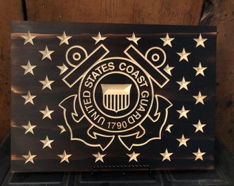 May include: A wooden sign with a carved image of the United States Coast Guard emblem. The emblem is surrounded by a circle of stars. The text "United States Coast Guard 1790" is carved into the emblem.