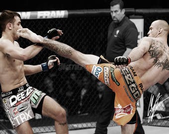 May include: Two men wearing athletic shorts and fighting in a mixed martial arts competition. One man is wearing black shorts with a green and white design and the other man is wearing orange shorts with a green and white design. The man in the orange shorts is kicking the man in the black shorts.