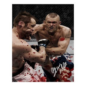 Puede incluir: Una imagen de acción de una pelea de artes marciales mixtas. Dos luchadores sin camisa están en combate, con salpicaduras de sangre visibles. Un luchador lleva guantes negros y el otro tiene un tatuaje. La imagen está firmada.