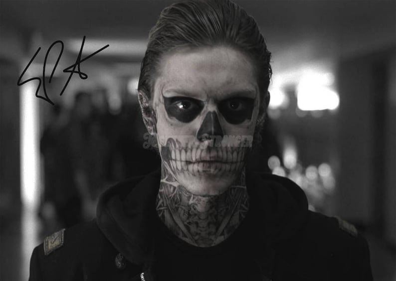 May include: Black and white photo of a person with a skull face paint and tattoos. The person is wearing a black hooded jacket.