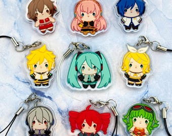 May include: A collection of nine anime-style character charms. Each charm features a different character with unique hair colors and outfits. The charms are made of clear acrylic and have a silver-colored clasp and a black lanyard for attachment.