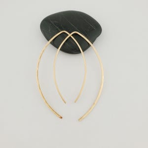 May include: A pair of gold hammered hoop earrings. The earrings are made of a thin wire and have a simple, elegant design.