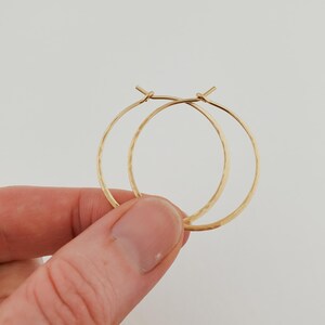 May include: A pair of gold-colored hoop earrings with a hammered texture. The earrings are round and have a simple, elegant design. The hoops are held together by a small clasp.