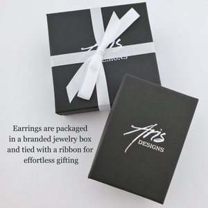 Earrings are packaged in a matte black jewelry box with Aris Designs logo stamped in metallic silver and tied with a white ribbon.