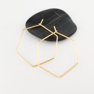 May include: A pair of gold hexagonal hoop earrings. The earrings are simple and modern in design.