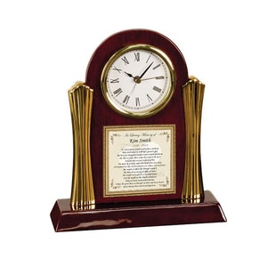 May include: A mahogany wood clock with gold accents and a white face. The clock has a plaque with the text "In Loving Memory of Kim Smith 1979-2021" and a poem.