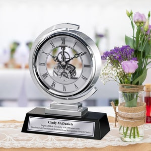 May include: Silver desk clock with a black base and an engraved plaque that reads "Cindy McDaniels Engraved Desk Clocks by AllGiftFrames.com Distributor of Personalized Retirement and Recognition Award Clocks".