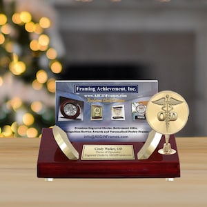 May include: A wooden desk display with a gold-colored emblem featuring the letters "OD" and a medical symbol. The display also includes a business card and a nameplate. The text on the nameplate reads "Cindy Walker, OD Doctor of Optometry".