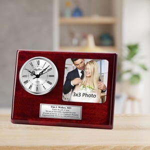 May include: A mahogany desk clock with a silver face and a 3x3 inch photo frame. The clock has a personalized plaque with the text "Tim J. Walker, MD Enjoy the gift of time We are so incredibly thankful for 10 years of service at LA Children's Hospital Engraved Desk Clocks by AllGiftFrames.com".