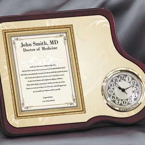May include: A mahogany-colored wooden plaque with a gold-framed certificate and a clock. The certificate reads "John Smith, MD Doctor of Medicine" and includes a medical symbol and a poem. The clock has a white face with black numbers and hands.