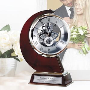May include: A silver and wood clock with a skeletonized movement. The clock is on a wooden base with a personalized plaque that reads "Kimberly T. Walker Engraved Desk Clocks by AllGiftFrames.com Distributor of Personalized Clocks".