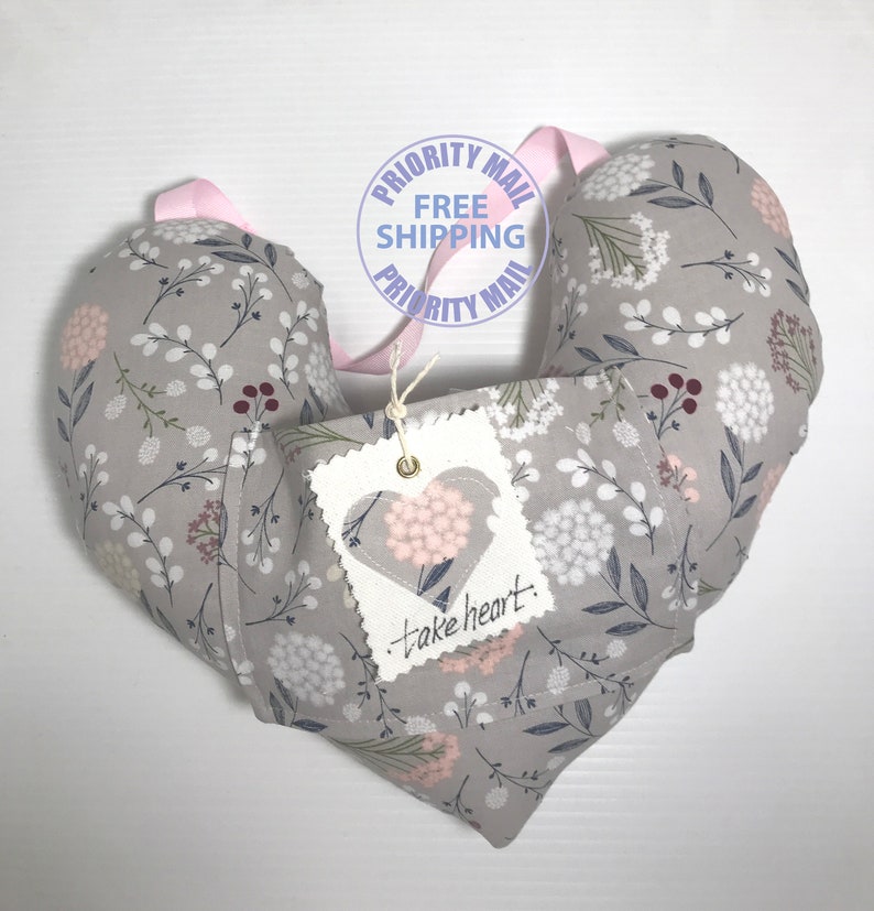 May include: A gray heart-shaped pillow with a floral pattern. The pillow has a tag attached that says "take heart".