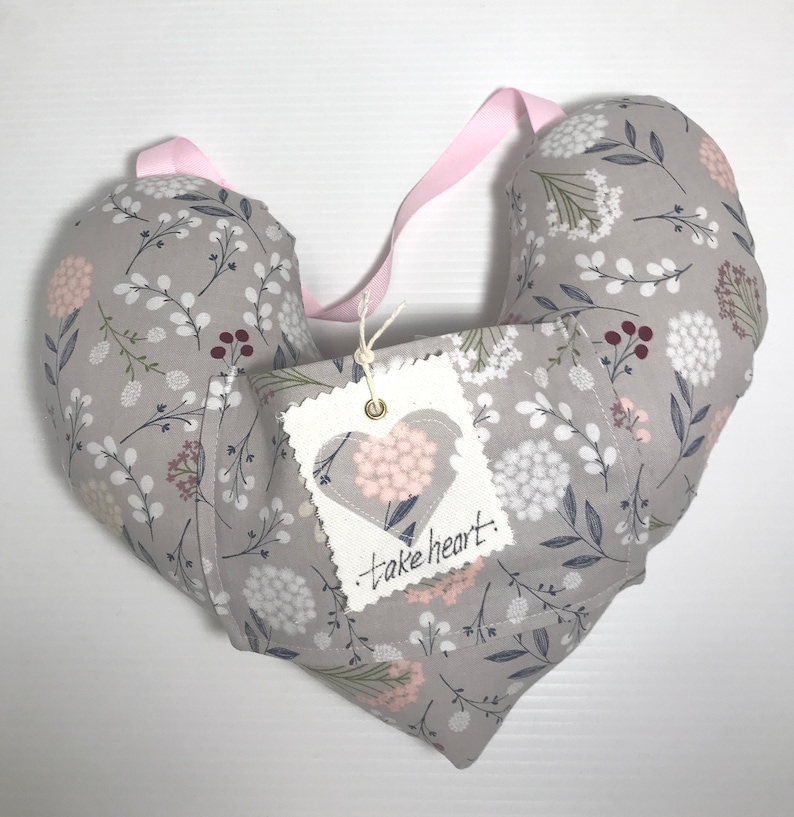 May include: A gray heart-shaped pillow with a floral pattern and a white tag that says "take heart".