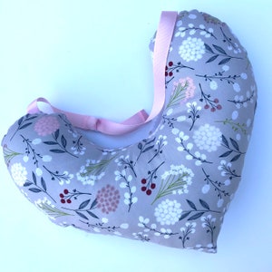 May include: A gray and white floral print pregnancy pillow with a pink strap. The pillow is shaped like a crescent moon and is designed to support the body during pregnancy.