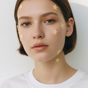 May include: A portrait of a person with short brown hair and light skin. Small yellow star stickers are placed on the face and neck. The person is wearing a white t-shirt.