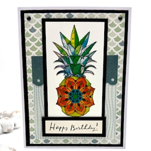 May include: A handmade birthday card featuring a colorful pineapple design. The pineapple has a green, blue, and yellow crown, with an orange and red floral body. The card includes the text "Happy Birthday!" in black script.