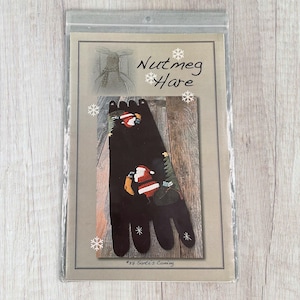 May include: A pattern for a felt Christmas stocking with a Santa Claus design. The pattern is titled "Nutmeg Hare #32 Santa's Coming".