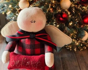 May include: A handcrafted angel doll with a cream-colored head, beige wings, and a red and black plaid dress. The doll holds a red pillow with the word "believe" embroidered on it. The angel is decorated with a black bow with red trim.