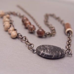 May include: A silver chain necklace with brown, white, and black stone beads. The necklace features a large, oval-shaped black stone with white veins.