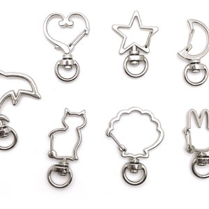 May include: Set of eight silver metal keychains with different shapes, including a heart, star, moon, dolphin, cat, flower, and rabbit.