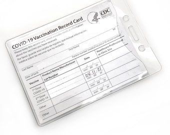 Puede incluir: Un portatarjetas de vacunación de plástico transparente con una tarjeta de registro de vacunación COVID-19 en su interior. La tarjeta tiene texto en inglés y español, incluyendo "COVID-19 Vaccination Record Card". El soporte tiene tres agujeros en la parte superior para un cordón. La tarjeta mide aproximadamente 10 cm x 7,6 cm.