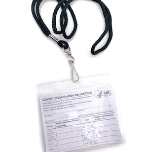 May include: A clear plastic card with a black lanyard. The card is a COVID-19 Vaccination Record Card with spaces to record the vaccine name, lot number, date, and healthcare professional or clinic site. The card also includes the CDC logo.