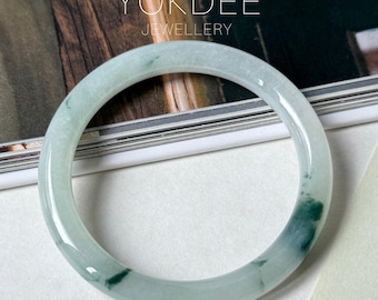 May include: A translucent jade bangle bracelet with areas of deep green and pale green hues. The bracelet is circular and smooth, with the text "YOKDEE JEWELLERY" in the background.