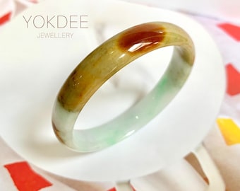 May include: A jade bangle bracelet with a green, white, and brown color scheme. The bangle is smooth and polished, and it has a slightly oval shape.
