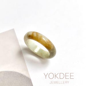 May include: A jade ring with a polished finish. The ring displays a mix of colours, including light green, yellow, and brown. The ring is set against a white background. The text "YOKDEE JEWELLERY" is visible.
