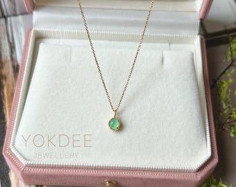 Op de afbeelding: Een delicate gouden ketting met een kleine, ronde, lichtgroene cabochon edelsteen hanger in een gouden rand met kraalmotief. Het sieraad wordt gepresenteerd in een lichtroze doosje met de tekst YOKDEE JEWELLERY aan de binnenzijde.