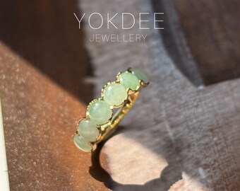 May include: A gold ring featuring a series of light green, round gemstones. The ring's band is a bright gold color, and the gemstones are evenly spaced along the top. The text "YOKDEE JEWELLERY" is visible in the background.