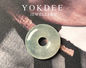 May include: A light green jade donut pendant with a hole in the centre. The pendant is on a dark background.