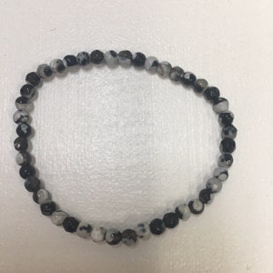 May include: Black and white agate beaded bracelet. The beads are round and have a speckled pattern.