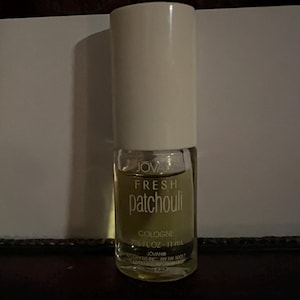 May include: A clear glass cologne bottle with a white cylindrical cap. The label reads JOVAN FRESH patchouli COLOGNE 0.376 FL OZ 11 mL JOVAN COTY US INC NY NY 10017. The bottle contains a light yellow liquid and has a cylindrical shape.