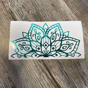 May include: A teal and black mandala design on a white background. The mandala is a decorative design with intricate details and a floral pattern.