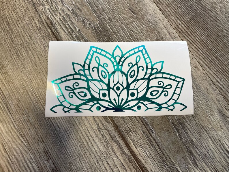 May include: A teal and black mandala design on a white background. The mandala is a decorative design with intricate details and a floral pattern.