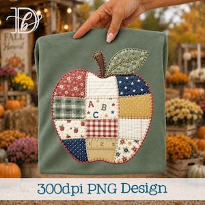 May include: A sage green t-shirt featuring a large, central apple-shaped appliqué made of various fabric patches. The patches include patterns like red gingham, blue stars, floral prints, and a ruler graphic. The center features the letters ABC.