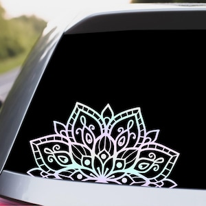 May include: A white mandala decal with a rainbow gradient on a black car window. The mandala is a circular design with intricate details.