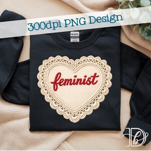 May include: A black sweatshirt featuring a heart-shaped design with the word "feminist" in red script. The heart is framed by a cream-colored, lace-like border. The text "300dpi PNG Design" is displayed across the top.