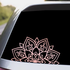May include: A pink and white mandala design decal on a black car window.
