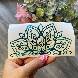 May include: A teal green mandala design on a white background. The mandala is a circular pattern with intricate details and a floral motif.