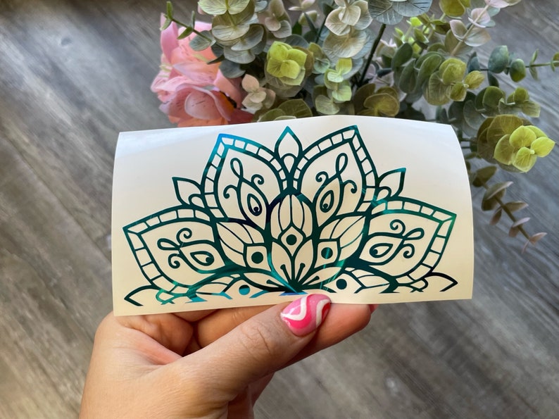 May include: A teal green mandala design on a white background. The mandala is a circular pattern with intricate details and a floral motif.
