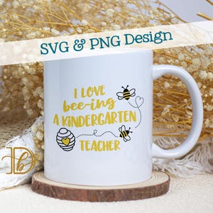 Może przedstawiać: Biały ceramiczny kubek z uchwytem, z napisem "I LOVE bee-ing A KINDERGARTEN TEACHER" w kolorze żółtym i czarnym. Projekt zawiera ilustracje pszczół i serce. Kubek stoi na drewnianej podstawce.
