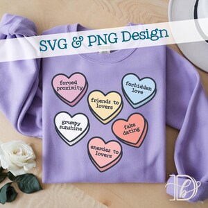 May include: A lilac sweatshirt adorned with heart-shaped candies, each bearing a phrase such as "friends to lovers" and "forbidden love." The text "SVG & PNG Design" is displayed. A white rose and a hat are visible in the background.