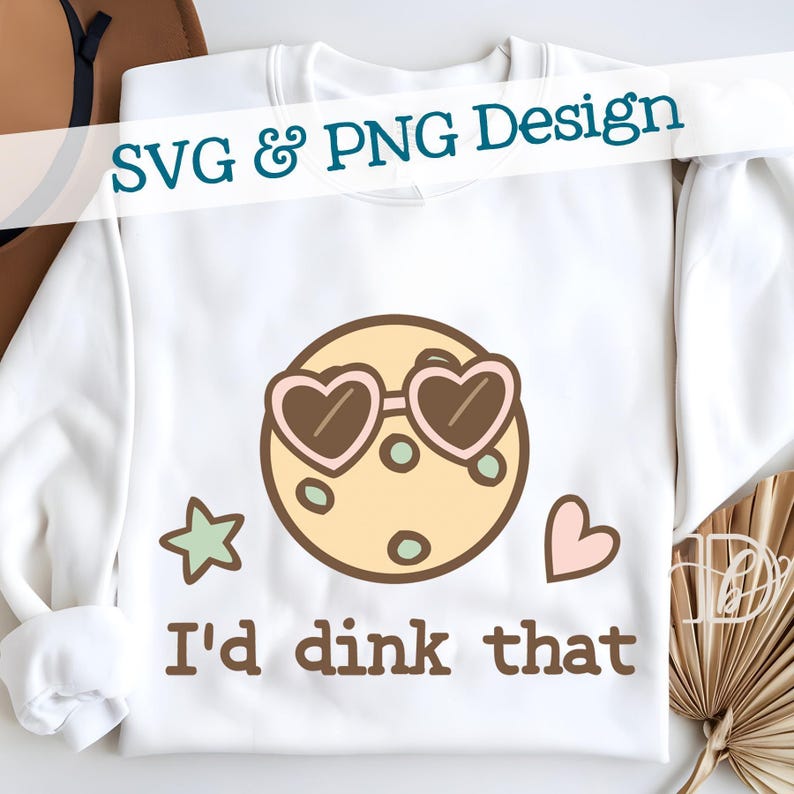 May include: White sweatshirt with a graphic design featuring a cartoon planet wearing heart-shaped sunglasses. The text "I'd dink that" is printed below the planet. The words "SVG & PNG Design" are printed across the top.